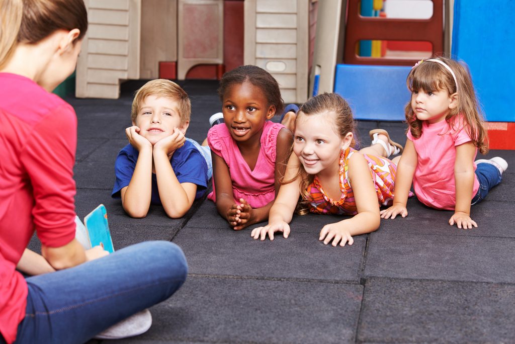 Nursery teacher reading story book to group of kids in kindergarten