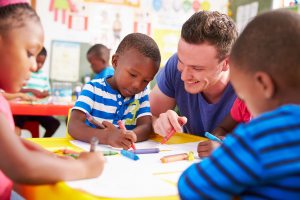 Male early childhood education teacher helping class