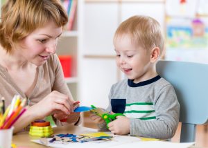 Woman teaches child handcraft at kindergarten or playschool or h